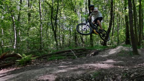 A-follow-up-shot-of-an-adult-male-jumping-on-an-electric-bicycle-on-trails-in-the-forest-on-at-sunny-day-in-slow-motion