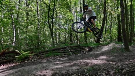 a follow-up shot of an adult male jumping on an electric bicycle on trails in the forest on at sunny day in slow motion