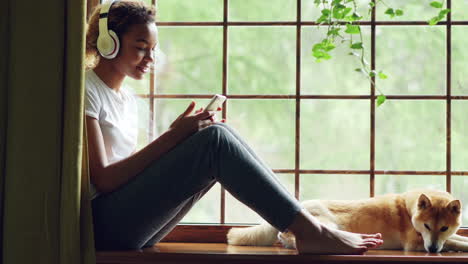 teen girl with headphones and phone on window sill with dog
