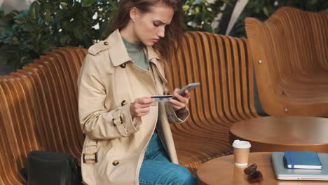 estudiante caucásica usando un teléfono inteligente y bebiendo café al aire libre.