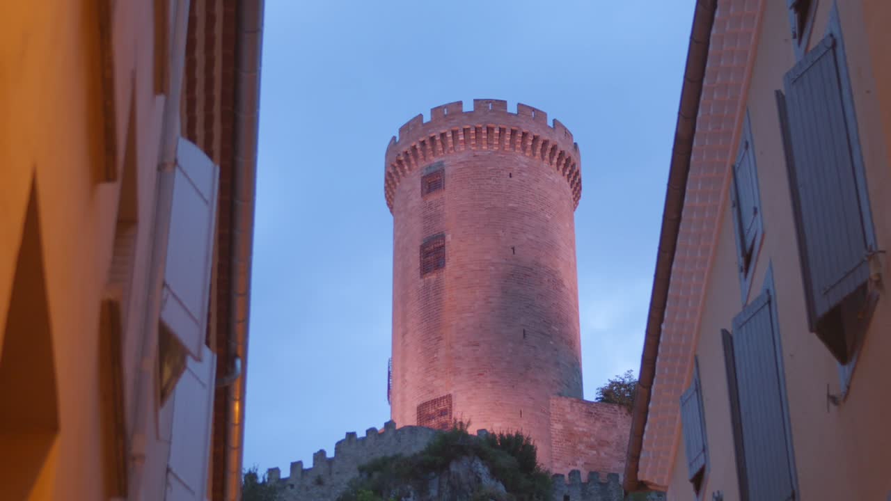 View of the illuminated medieval castle of Foix at twilight, framed by old town buildings
