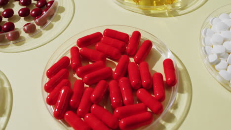 video de cerca de una variedad de pastillas y cápsulas en platos de vidrio sobre un fondo amarillo.