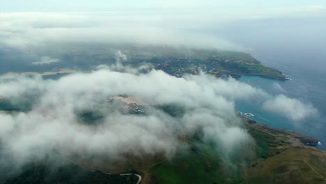 Drone-flying-over-clouds-revealing-Ajo-scenic-Coastline,-Aerial-High-view