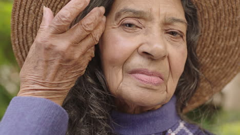 Primer-Plano-Retrato-De-Una-Anciana-India-Mirando-La-Cámara-Arreglando-El-Cabello-Con-Sombrero