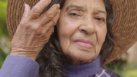 retrato en primer plano de una mujer india de edad avanzada mirando a la cámara arreglando el cabello con sombrero