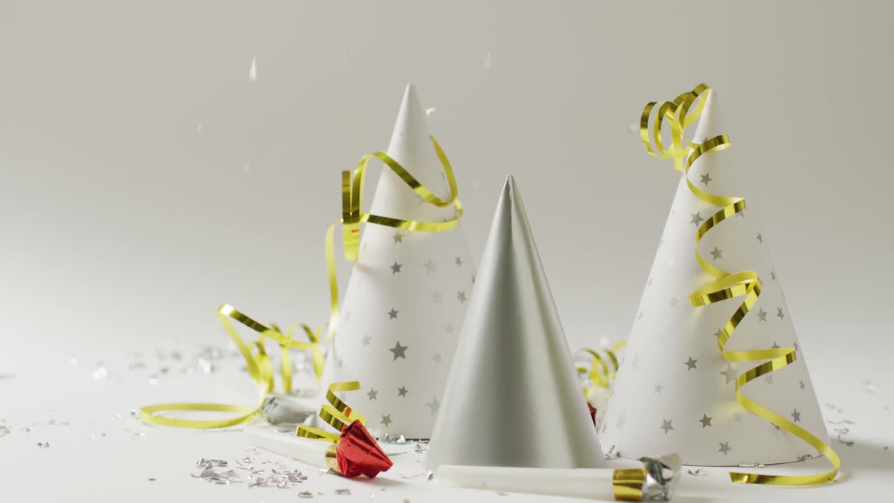 video de tres sombreros de fiesta blancos y plateados con serpentinas de oro y confeti de plata en gris pálido