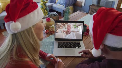 Caucasian-couple-with-santa-hats-using-laptop-for-christmas-video-call-with-woman-on-screen