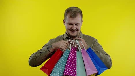 Man-showing-Black-Friday-inscription-on-shopping-bags,-smiling,-satisfied-with-low-prices-purchases