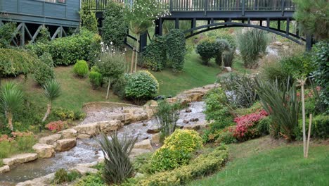 a tranquil stream flows through a beautifully landscaped garden with a wooden bridge