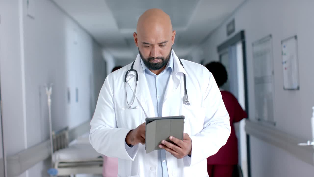 Ritratto di felice dottore di origine mista in camice da laboratorio, che usa un tablet nel corridoio, al rallentatore.