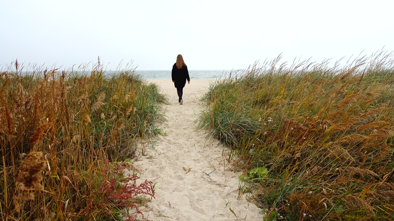 Pigen går på stranden ad en sti. Optagelse om efteråret