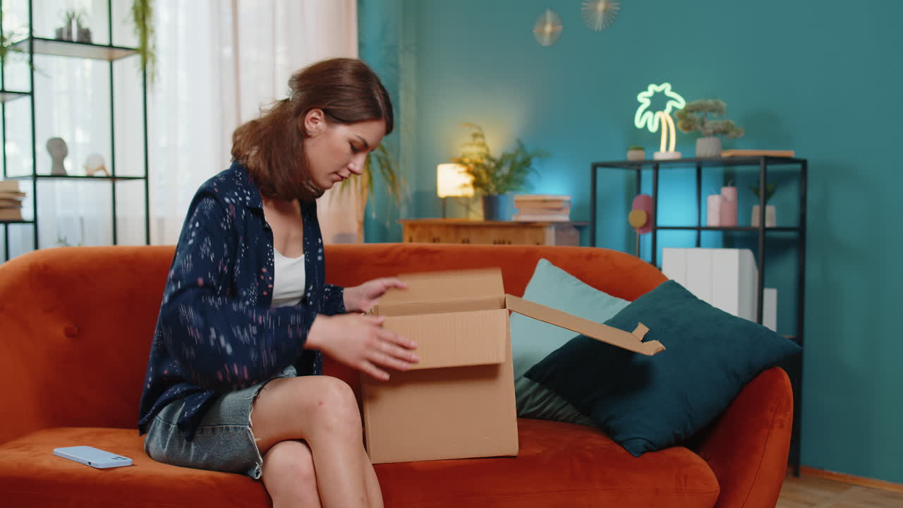 una mujer infeliz desempaquetando una caja de cartón se siente insatisfecha con un pedido de auriculares inalámbricos dañados y rotos.