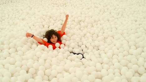 una linda niña de 9-10 años divirtiéndose entre un montón de bolas blancas en un pozo de bolas. 4k cámara lenta
