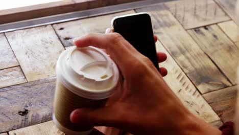hombre usando teléfono móvil mientras toma una taza de café