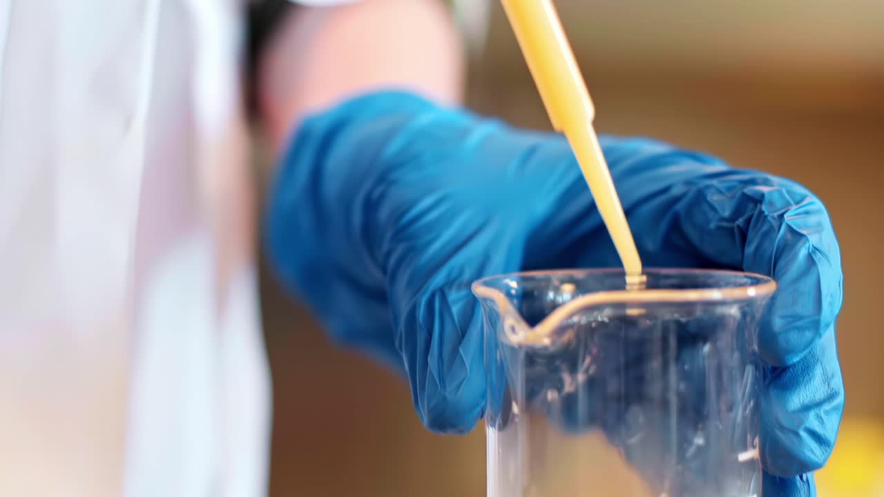 Primo piano di un liquido prelevato con una pipetta e fatto cadere in una capsula di Petri in un ambiente di laboratorio.