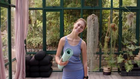 smiling woman holding yoga mat in glass house, ready for yoga session