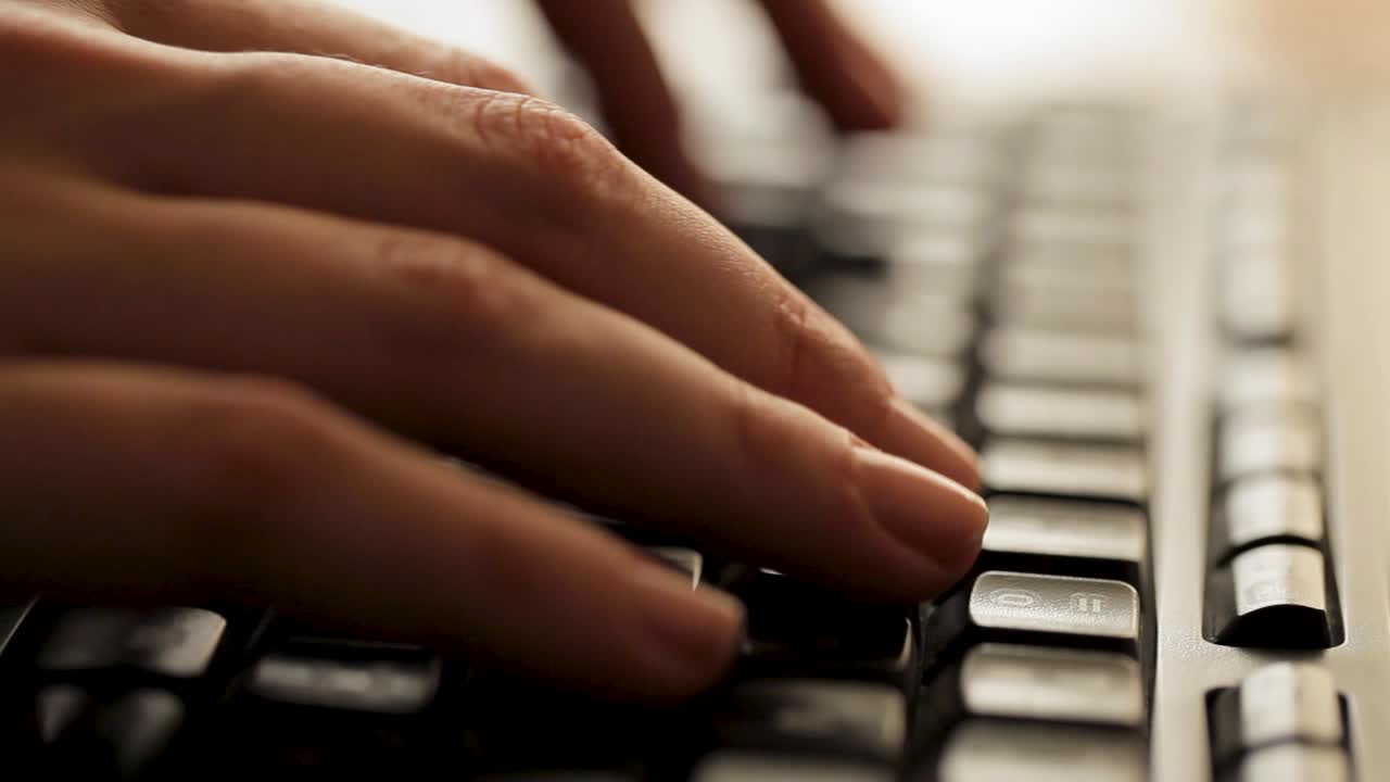 Close-up of fingers typing quickly on a backlit keyboard, focus on hands