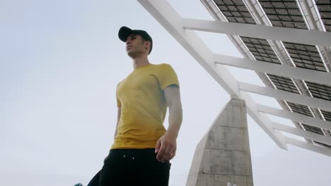 Young-Attractive-Trendy-Man-walking-with-a-skateboard-under-a-solar-panel-on-a-morning-sunny-day-with-an-urban-city-background-in-slow-motion