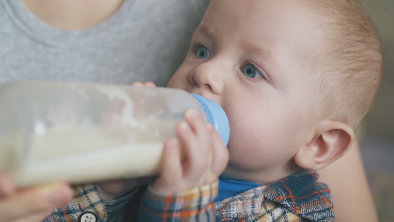 il ragazzino mangia una miscela di latte dalla bottiglia tra le braccia della mamma