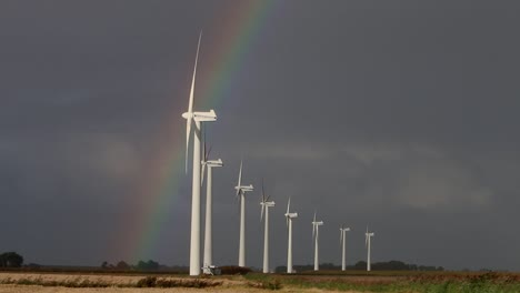 a line of wind turbines turning on a windy day with a stormy sky and rainbow in the background