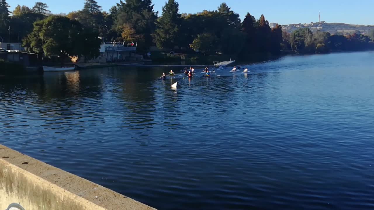 Group of kayakers rowing around a dam early one autumn morning. Still some mist over the water and trees are beginning to go yellow.  Emmarentia dam, Johannesburg Botanical Gardens, South Africa