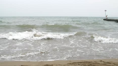 An-Einem-Sandstrand-Und-Mit-Einem-Steg-Kommen-Kleine-Wellen-Herein,-Aber-Das-Wetter-Ist-Nicht-So-Schön