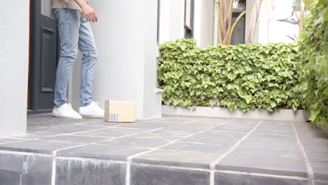 biracial man picking up delivery in cardboard box outside front door, copy space, slow motion