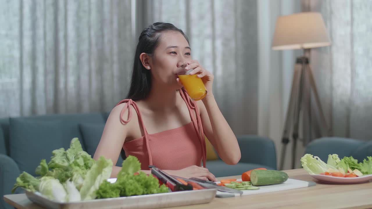 아시아 여성이 오렌지 주스를 마시고 집에서 건강한 음식을 먹는 동안 카메라에 미소 짓고 있습니다.