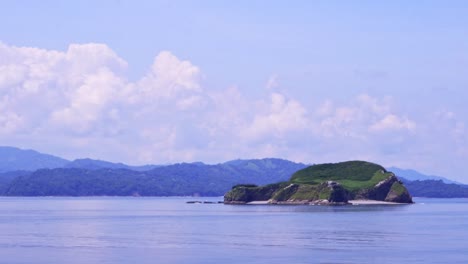 passing island with mountains on the horizon in costa rican landscape on sunny day with cloudy sky, close shot