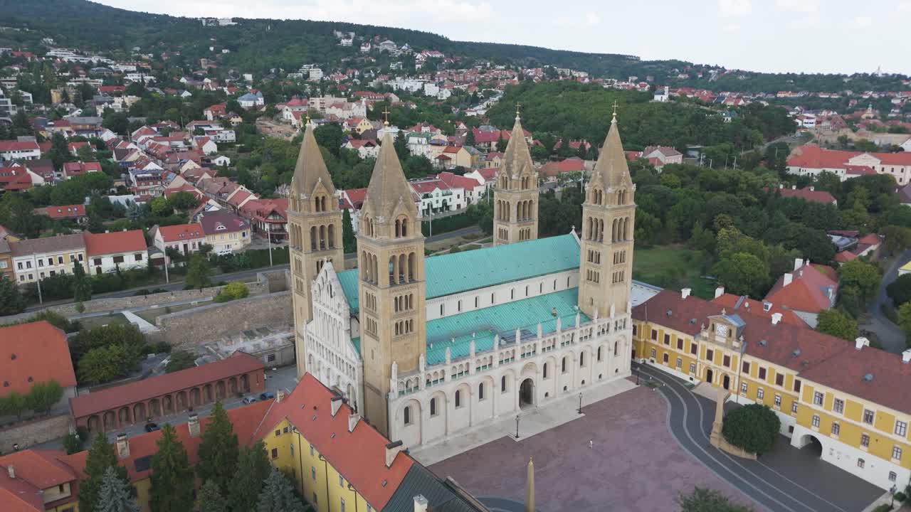 Drone orbiting Pécs Cathedral, highlighting its front facade, twin towers, and architectural details