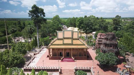 Pagoda-whit-ancient-Khmer-Temple-in-lush-green-countryside-drone-lift-revealing-large-reclining-Buddha---Kampong-Cham,-Cambodia