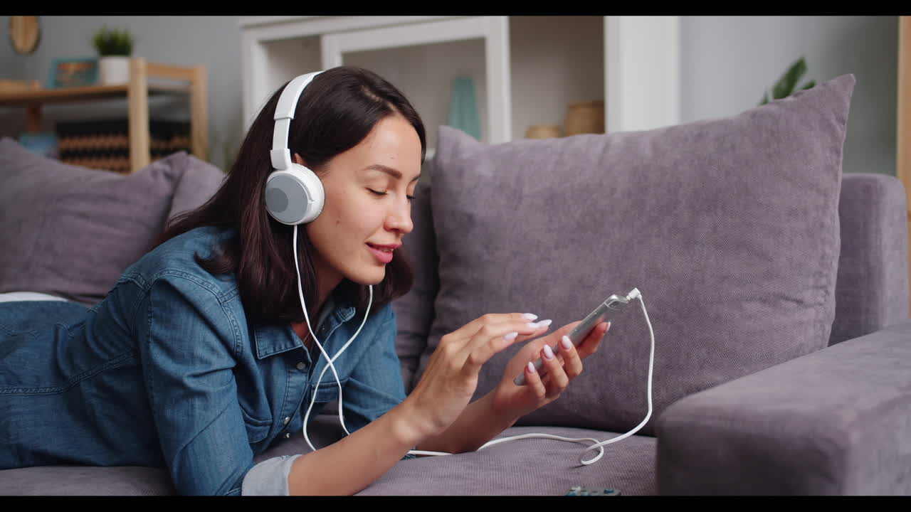 여성이 헤드폰과 전화로 소파에서 휴식을 취하고 있습니다.
