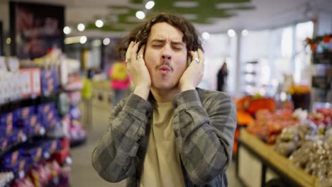 Happy-brunette-guy-with-curly-hair-and-headset-listens-to-cheerful-music-while-shopping-in-a-grocery-store