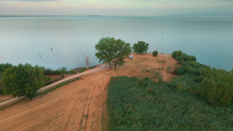 Autocaravana-Blanca-Estacionada-En-La-Punta-De-La-Orilla-Del-Lago-Durante-El-Amanecer-Con-Aguas-Tranquilas-Del-Lago-Trasimeno-En-Italia