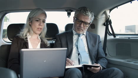 businessman making notes in notebook while the businesswoman holding laptop on knees