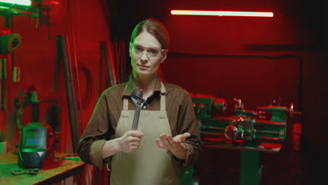 caucasian young female welder holding wrench in hand and looking at camera at work in workshop