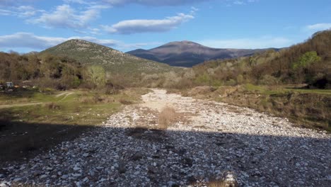 Low-aerial-flight-over-dry-river-bed-surrounded-by-mountains