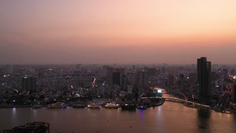 ho chi minh city, vietnam iconic skyline and saigon river waterfront aerial panning shot on a busy evening featuring key buildings illuminated against beautiful colored sky and reflected in the river