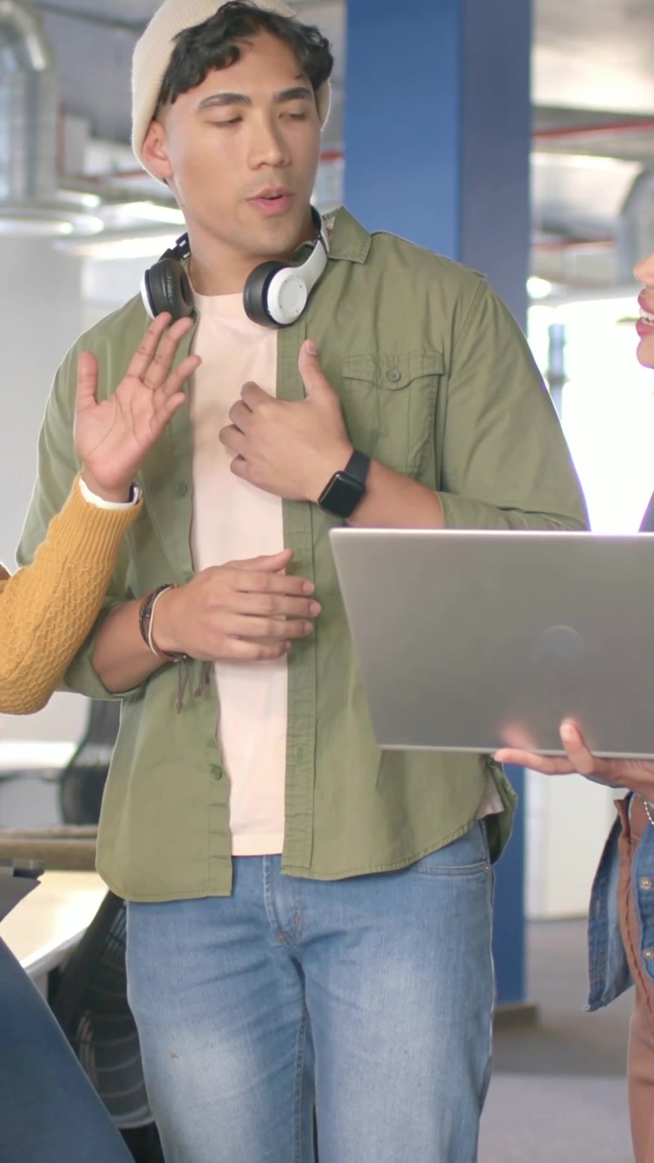 Video vertikal: Pria bereaksi terhadap isyarat tangan kiri, melihat laptop di kantor dengan topi kupluk dan headset.