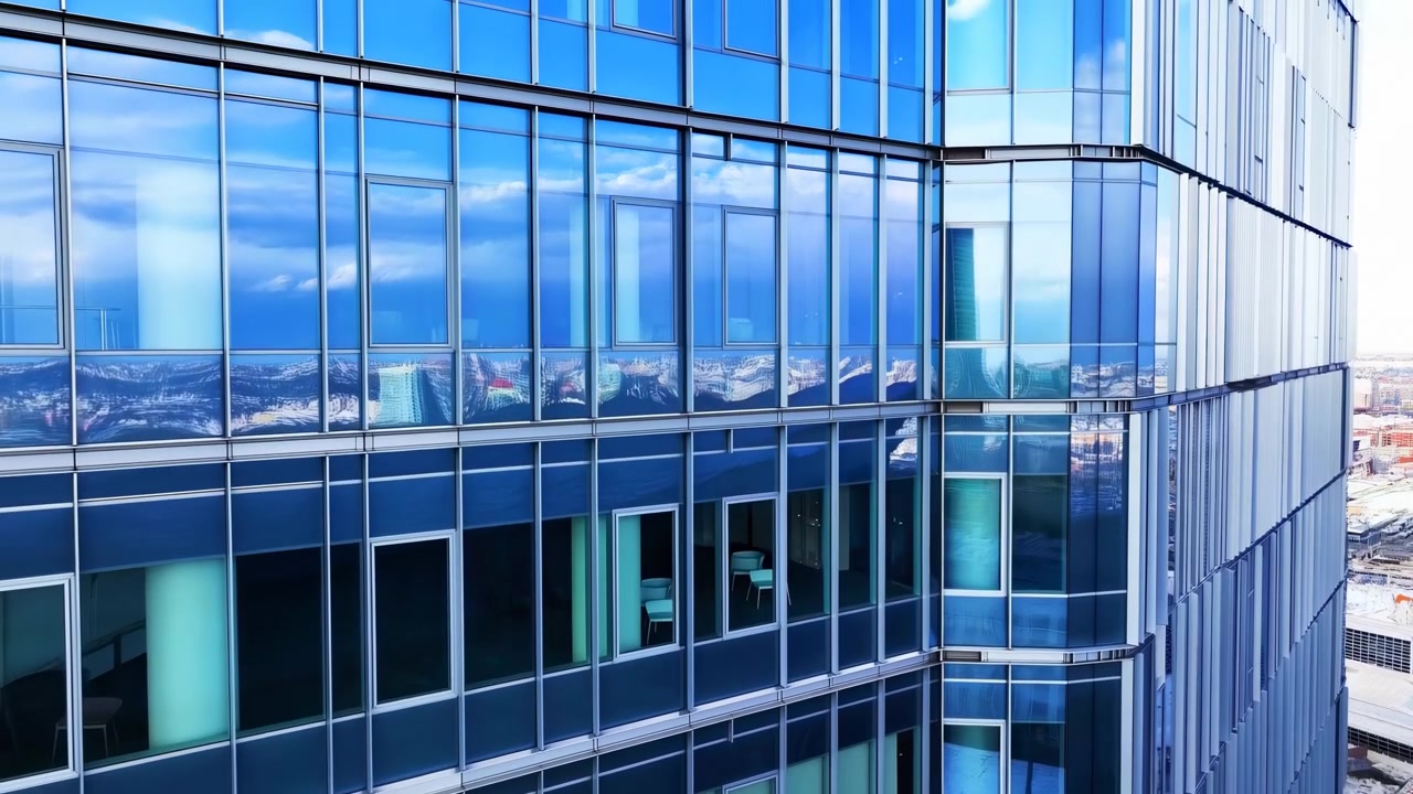 Vista arquitetônica detalhada de um canto de torre de escritório moderna, mostrando painéis de parede cortina refletivos com tonalidade azul, montantes metálicos e reentrâncias de janelas embutidas.