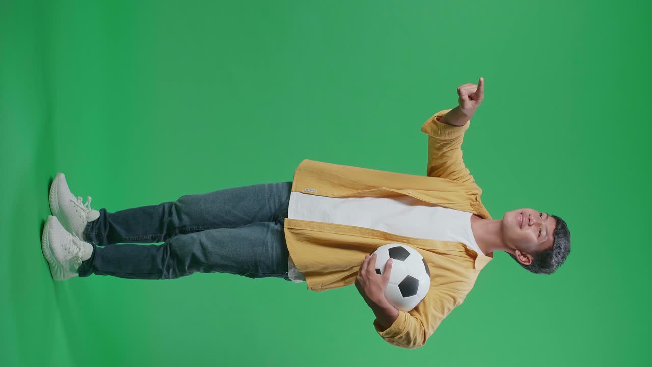 동양 소년이 공을 들고 가에 손을 고 앞을 가리키며 녹색 스크린 배경에서 축구를 응원하는 모습