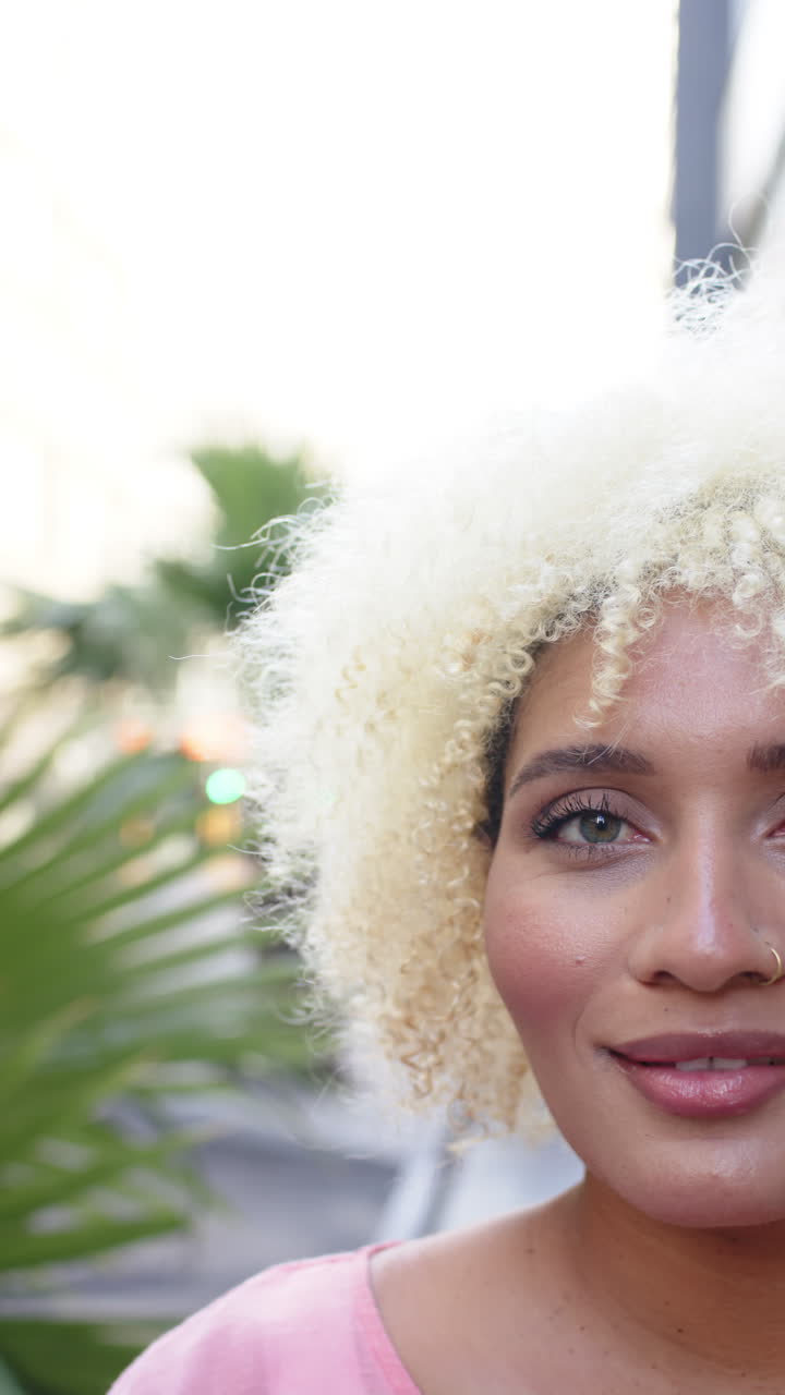 Vertical video: Smiling woman with curly hair enjoying outdoor cafe, looking at camera