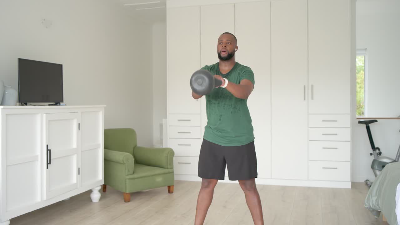 Uomo che inizia una serie di kettlebell oscillando il peso in avanti in un'area di allenamento in camera da letto, costruendo forza