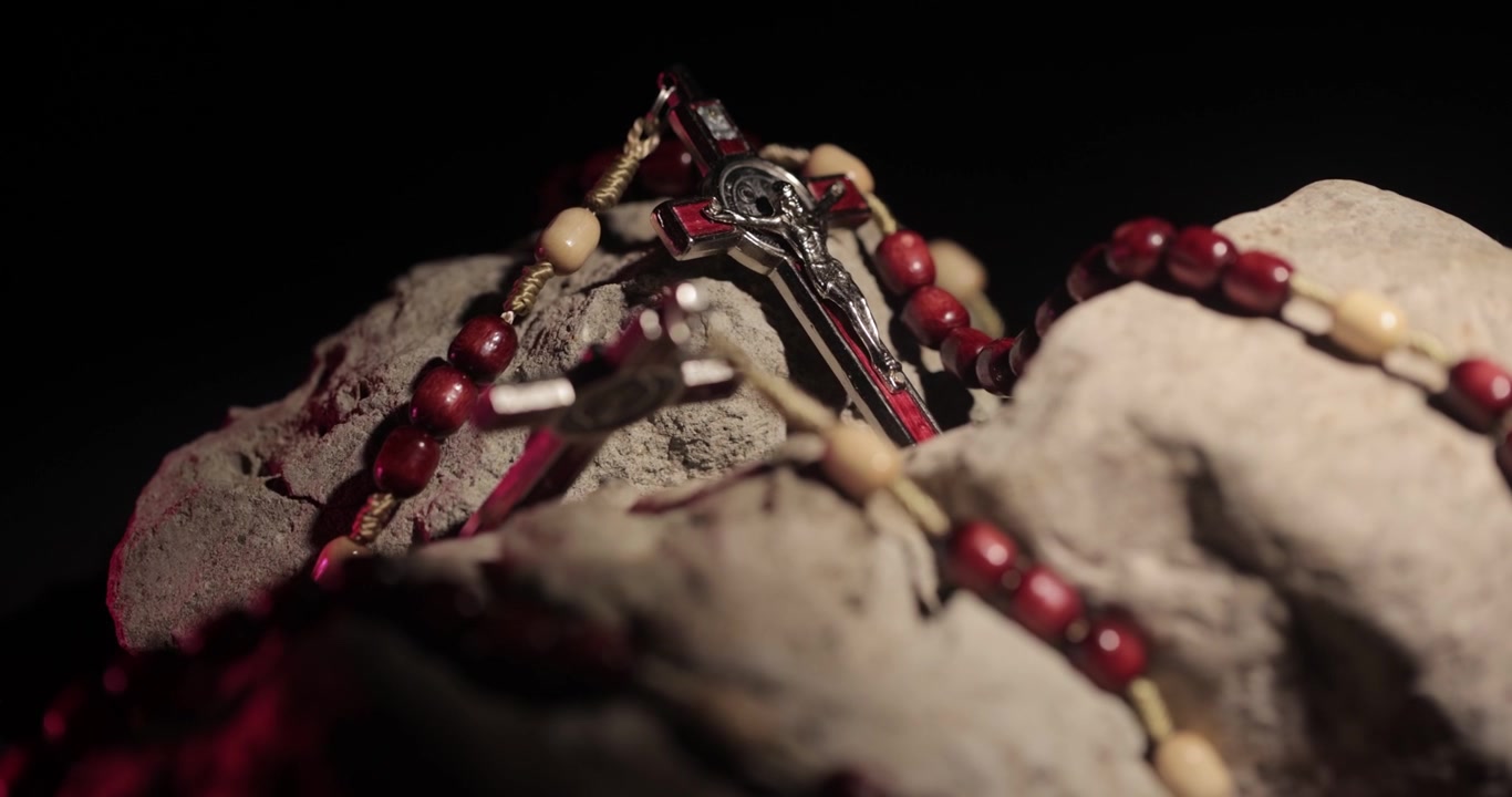 Ripresa cinematografica di prodotto di rosario rosso con simbolo di Gesù su pietre, 4K