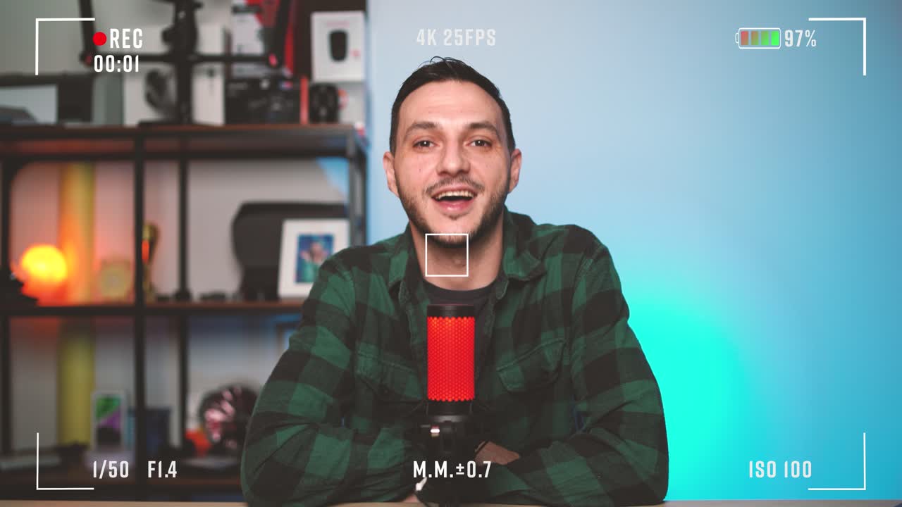 Cinematic footage of a male podcaster talking confidently into a microphone during live recording. Visible camera overlay interface showing rec symbol and sound levels