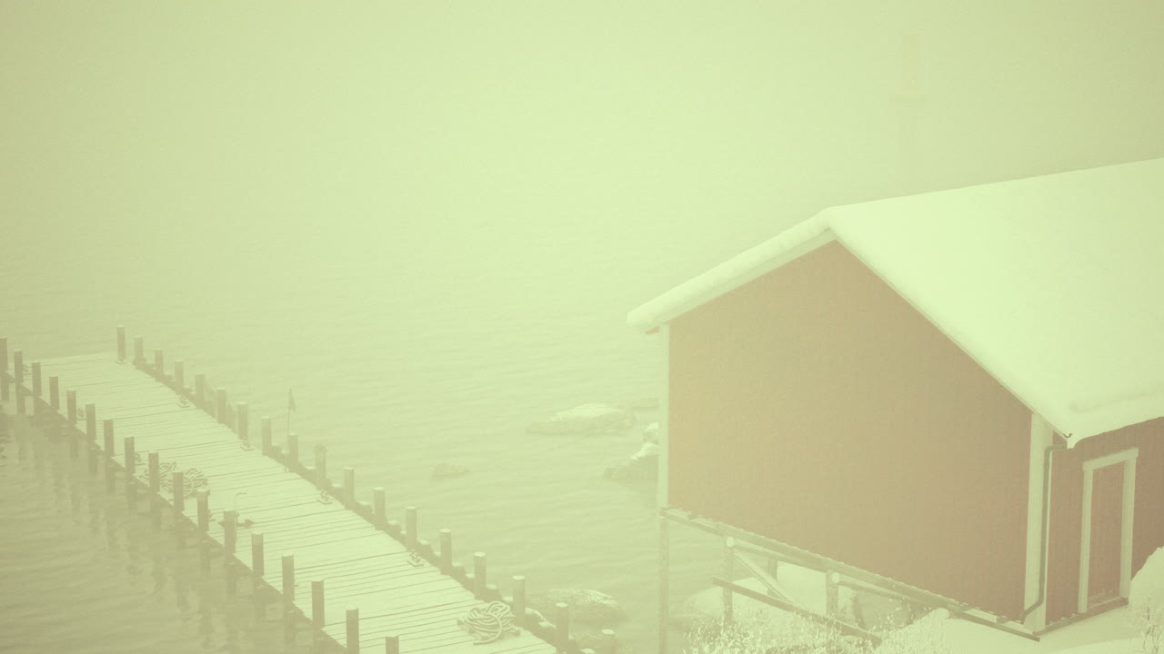 Snowy dock with red cabin shrouded in winter mist at calm lake