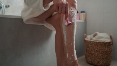 caucasian woman in bathrobe shaving her legs.