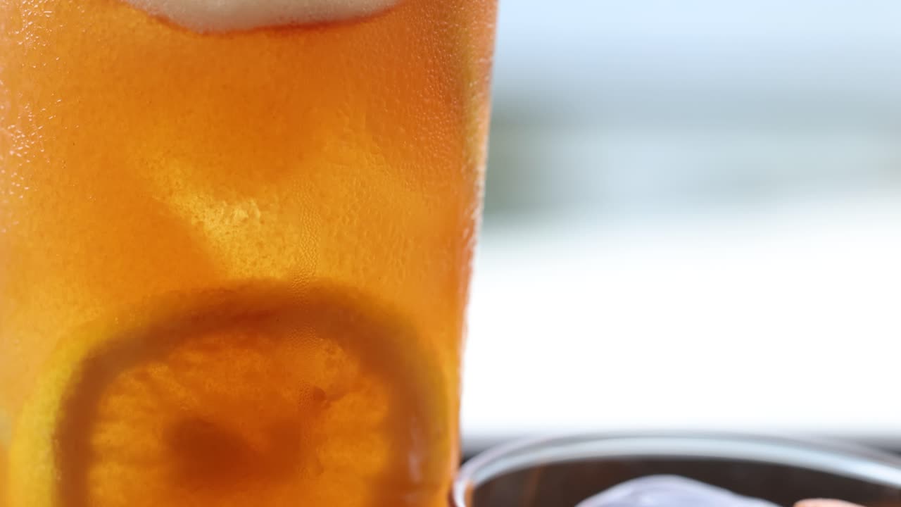 primer plano de un vibrante cóctel de cítricos adornado con hierbas frescas, mostrando condensación y hielo en un entorno brillante