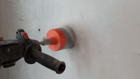primer plano del taladro con boquilla cilíndrica, trabajador de la construcción taladro pared de ladrillo enyesado, agujero en la pared, preparación para tirar del cableado eléctrico, partícula de ladrilo, trabajo de construcción en apartamento