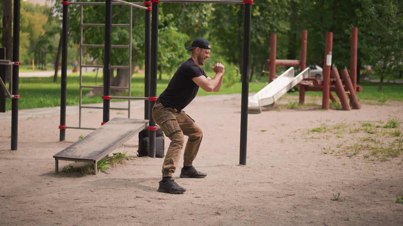 Focused Workout With Bodyweight Squats, Person Practicing Proper Squat Form Outdoors During Daylight, Male Engaging In Deep Squat Exercises Near Park Bench Emphasizing Technique And Stability
